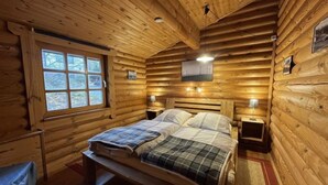 Camera da letto in baita di legno, con un letto, due comodini, una finestra e pareti in legno.