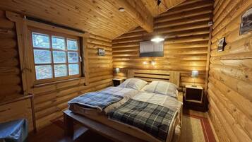 Ein Schlafzimmer in einer Blockhütte mit einem Bett, zwei Nachttischen, einem Fenster und Holzwänden.