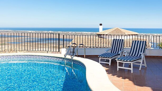 Ein Pool mit Blick aufs Meer, zwei gestreifte Liegestühle und eine geflieste Terrasse.