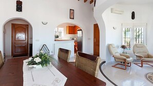 Ein geräumiges Wohnzimmer mit einem Holzessttisch, zwei Korbstühlen und einem weißen Sofa.
