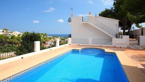 A swimming pool with a white building and a staircase leading to a balcony.