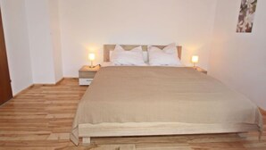 Un dormitori amb sòl de fusta, un llit amb roba de llit blanca, dues taules de nit amb làmpades i un quadre penjat a la paret.