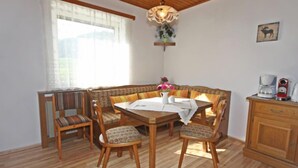 Una zona de menjador amb taula i caires de fusta, una banca, llum penjant i una cafetera sobre un moble.