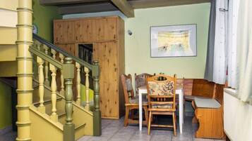 A staircase with wooden balusters, a dining area with wooden chairs and a table, and a framed picture on the wall.