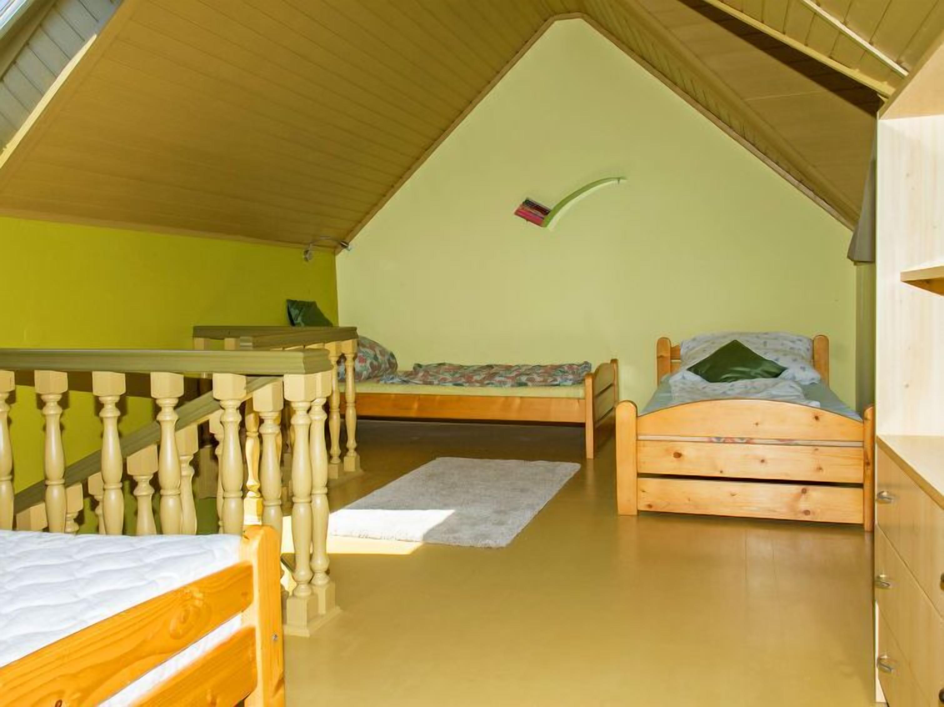 A dormitory room with two wooden beds, a wooden desk, and a bunk bed.