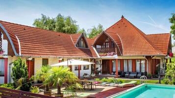 A two-story building with a red-tiled roof, a swimming pool, and outdoor seating.