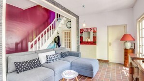 A living room with a grey sofa, a small round table, a red lamp, and a wall with a 'LONDON' sign.