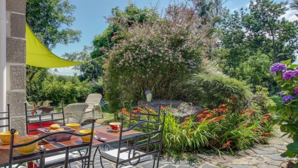 An outdoor patio with a table set for dining, surrounded by lush greenery and flowering plants.