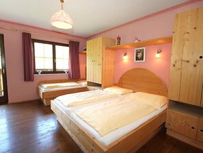 A bedroom with two wooden beds, a window with curtains, a wooden wardrobe, and a wall-mounted light fixture. - Christoph by Interhome (Kaltenbach)