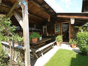 En træhytte med en overdækket terrasse, træbænke og plantede krukker.
