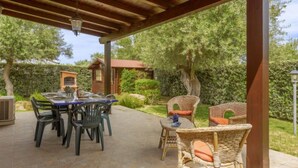 An outdoor patio with a wooden pergola, a table with chairs, and wicker furniture.