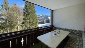 Een balkon met een tafel en bankje, met uitzicht op een besneeuwd berglandschap.