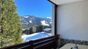 Een balkon met een houten hekwerk, een tafel met een kaars en uitzicht op besneeuwde bergen.