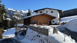 Een chalet met twee verdiepingen, een houten gevel, een overdekte veranda en uitzicht op besneeuwde bergen.