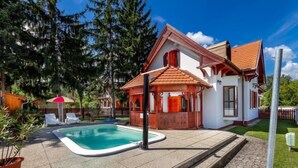 Ein Haus mit Schwimmbad, Holzterrasse und einer kleinen Laube.