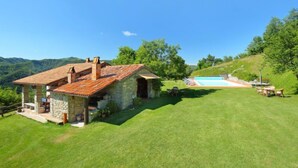 Una casa de piedra con techo de tejas, piscina y césped.
