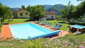 Una piscina con sillas de descanso, un jacuzzi y una casa al fondo.