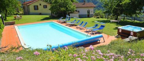 Piscina com espreguiçadeiras, uma banheira de hidromassagem e uma casa ao fundo.