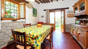 Un comedor con una mesa dispuesta para cuatro personas, sillas de madera, una pared de piedra, techo de madera y vistas al exterior a través de un ventanal.