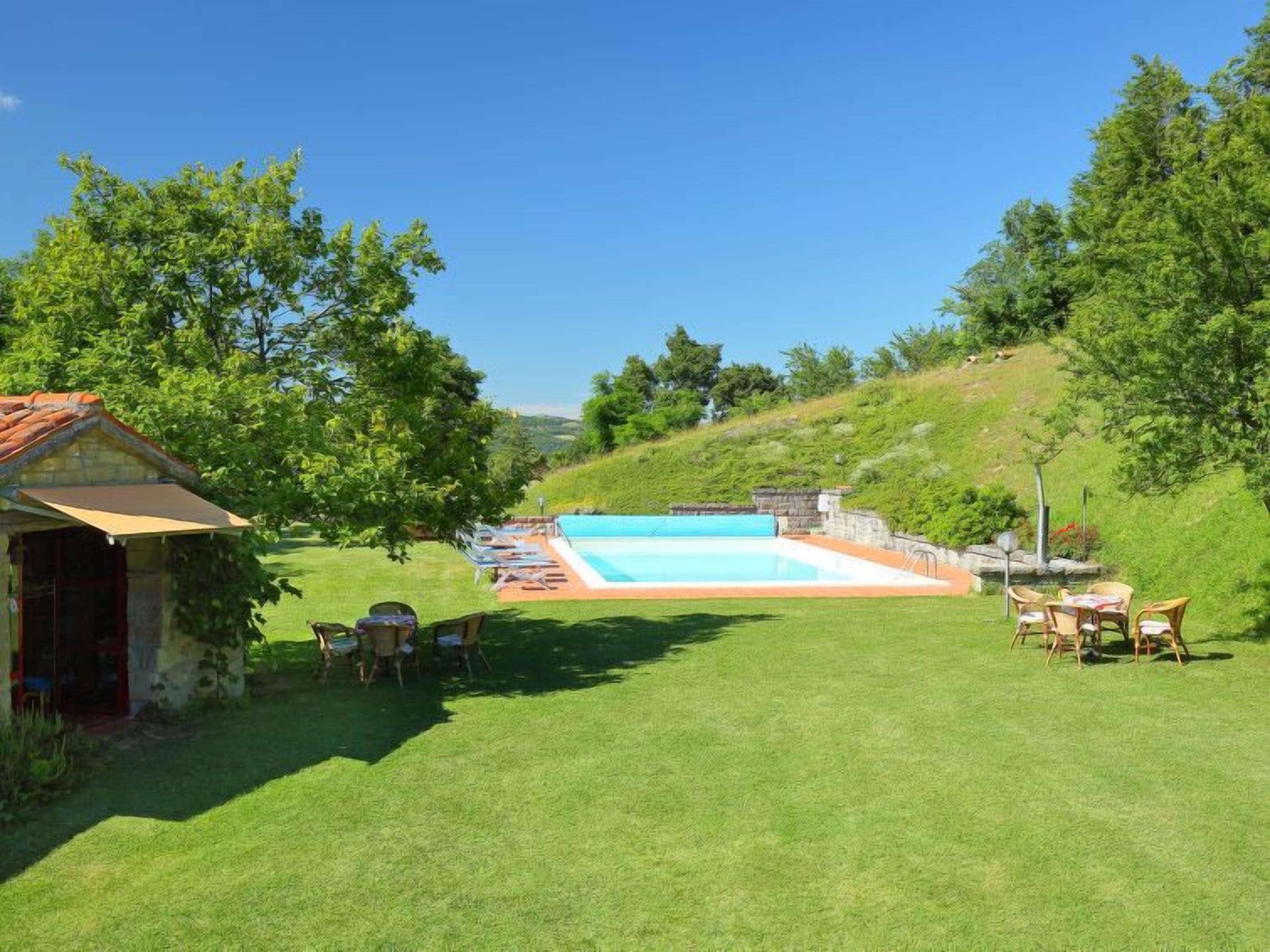 A backyard with a swimming pool, lawn chairs, and a small building.