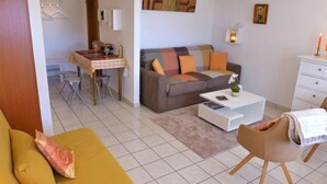A living room with a sofa, a coffee table, a dining area with a table and chairs, and a small kitchen area. - Valdor A 42 Sud by Interhome (Crans-Montana)