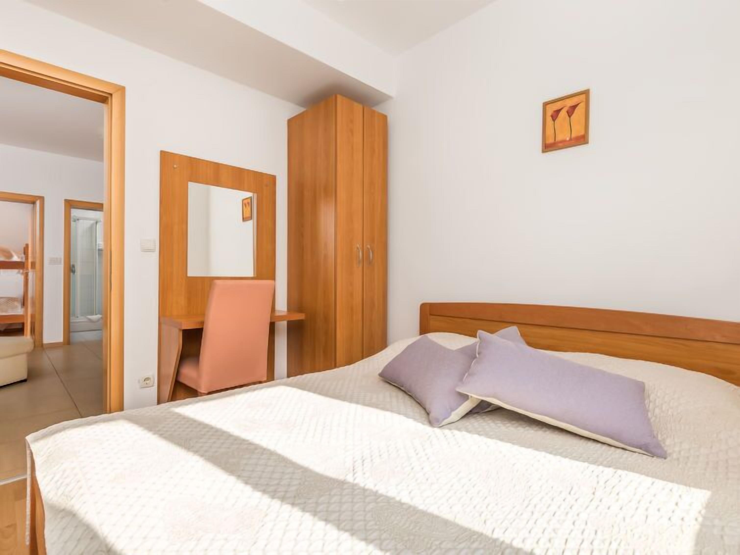 Una camera da letto con un letto, un armadio in legno, una scrivania con una sedia e una doccia sullo sfondo.