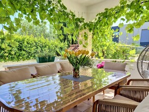 Un coin repas avec une table à plateau en verre, des chaises en osier et une plante en pot ornée de fleurs jaunes.