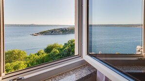 Vista costera a través de una ventana, con una isla rocosa y mar tranquilo.
