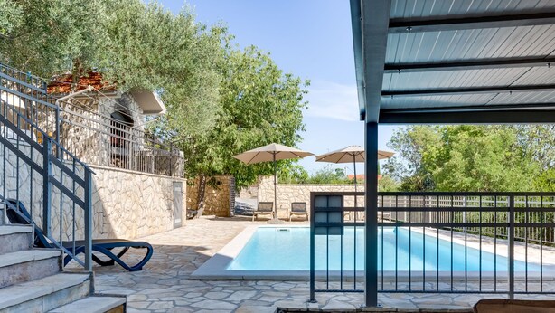 Une piscine avec des marches en pierre menant à son bord, entourée d’un mur de pierre et d’une rambarde en métal.