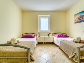 Een kamer met twee bedden, een raam en een schilderij aan de muur.