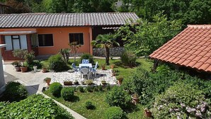 Ein Haus mit Ziegeldach, einer kleinen Terrasse mit Tisch und Stühlen sowie verschiedenen Kübelpflanzen.