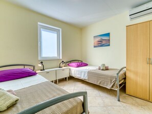 Een slaapkamer met twee bedden, een raam, een bureau, een kledingkast en een schilderij aan de muur.