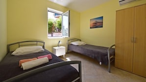 Ein Zimmer mit zwei Einzelbetten, einem kleinen Nachttisch mit Lampe, einem Fenster mit Blick auf Grünflächen und einem Kleiderschrank.