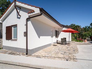 A white building with a stone patio, a red umbrella, and a door with shutters.