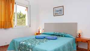 Une chambre à coucher avec un lit, deux tables de chevet, une fenêtre avec des rideaux et un tableau encadré au mur.