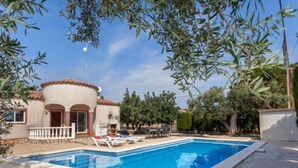 Une piscine avec des chaises longues, un bâtiment doté d’arcades et des arbres tout autour.