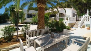 Een witte villa met een zwembad, omringd door palmbomen en een houten terras met zitplaatsen.