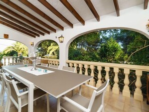 An outdoor dining area with a table and chairs, surrounded by a balustrade and a view of greenery.