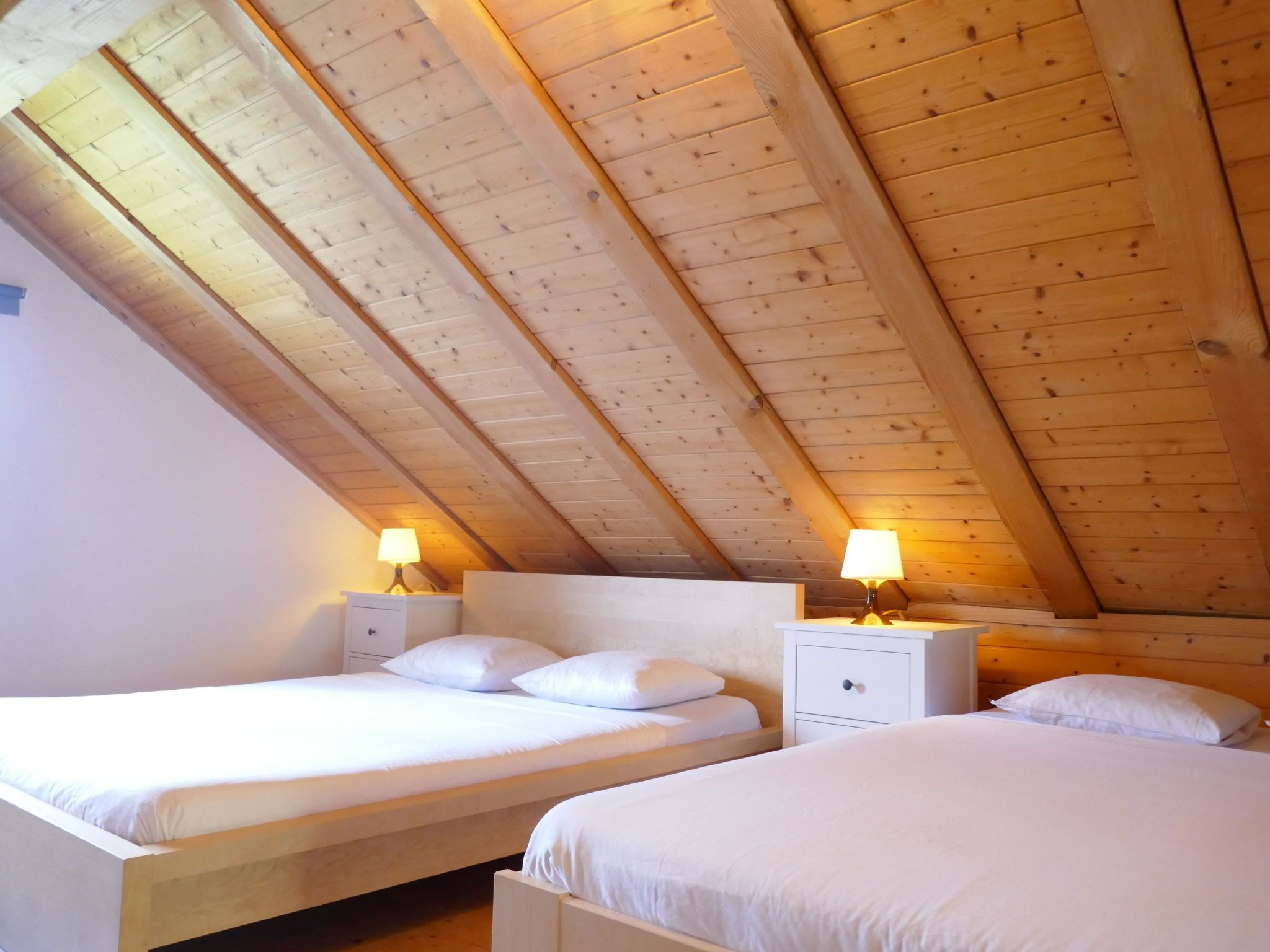 A room with two beds, wooden ceiling beams, and bedside lamps.