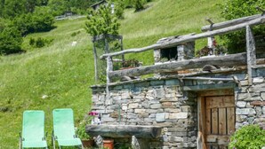 A rustic stone building with a wooden door, a wooden porch, and two green chairs in front. - Rustico Pamela by Interhome (Malvaglia)