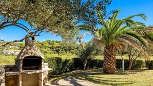 A stone-built outdoor kitchen area with a chimney, surrounded by well-maintained hedges and palm trees. - Mihaela 4 by Interhome (Rab/Rab)
