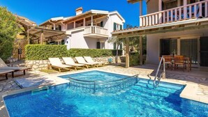 A swimming pool with lounge chairs and a dining area, surrounded by a landscaped garden and a multi-story building with balconies. - Mihaela 4 by Interhome (Rab/Rab)