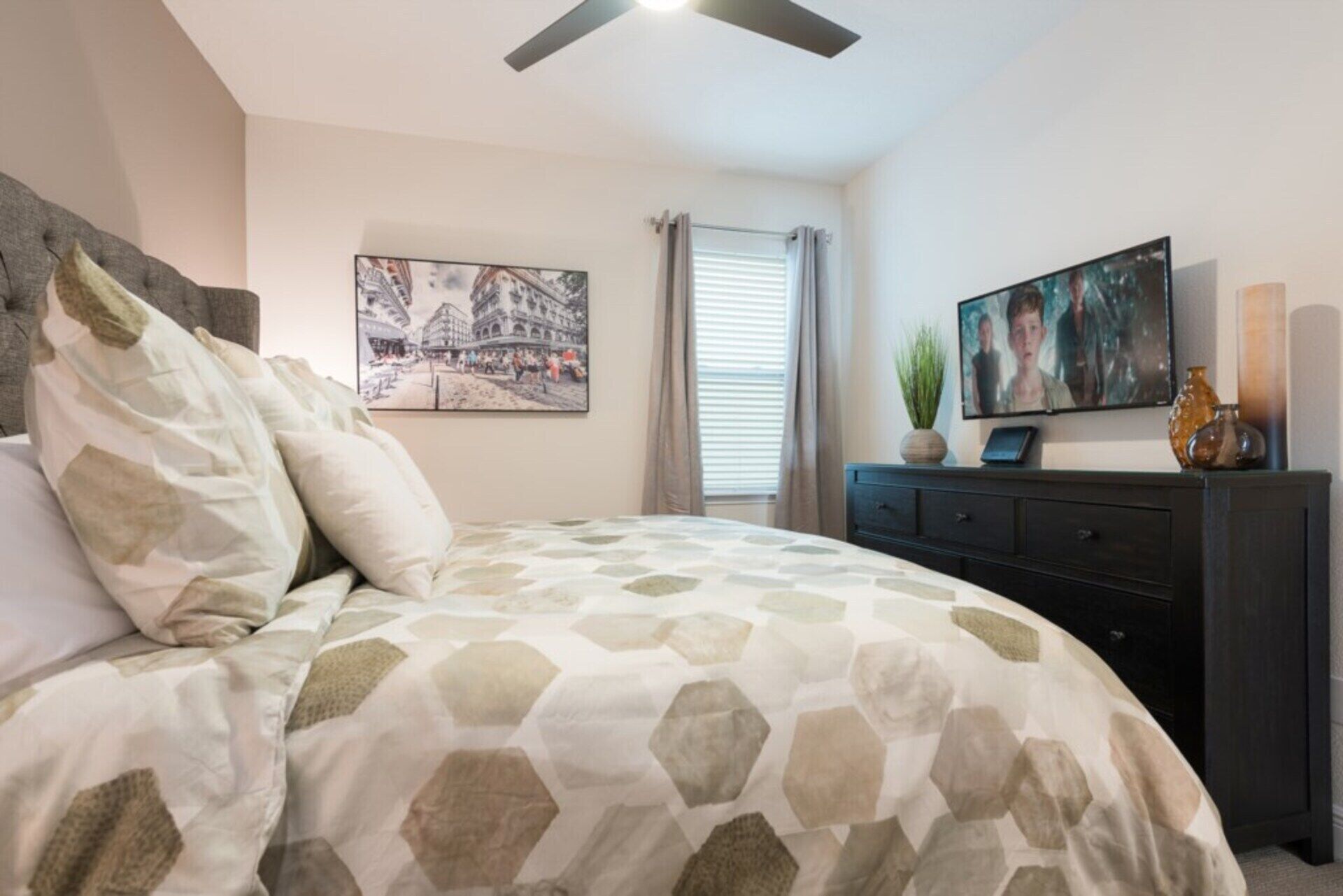 A bedroom with a bed, a dresser, a television, and a painting on the wall.