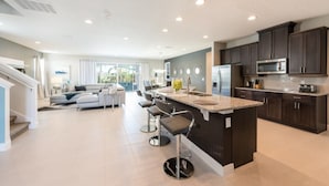 A modern kitchen with dark cabinets, a central island, and a dining area with a gray sofa and bar stools.