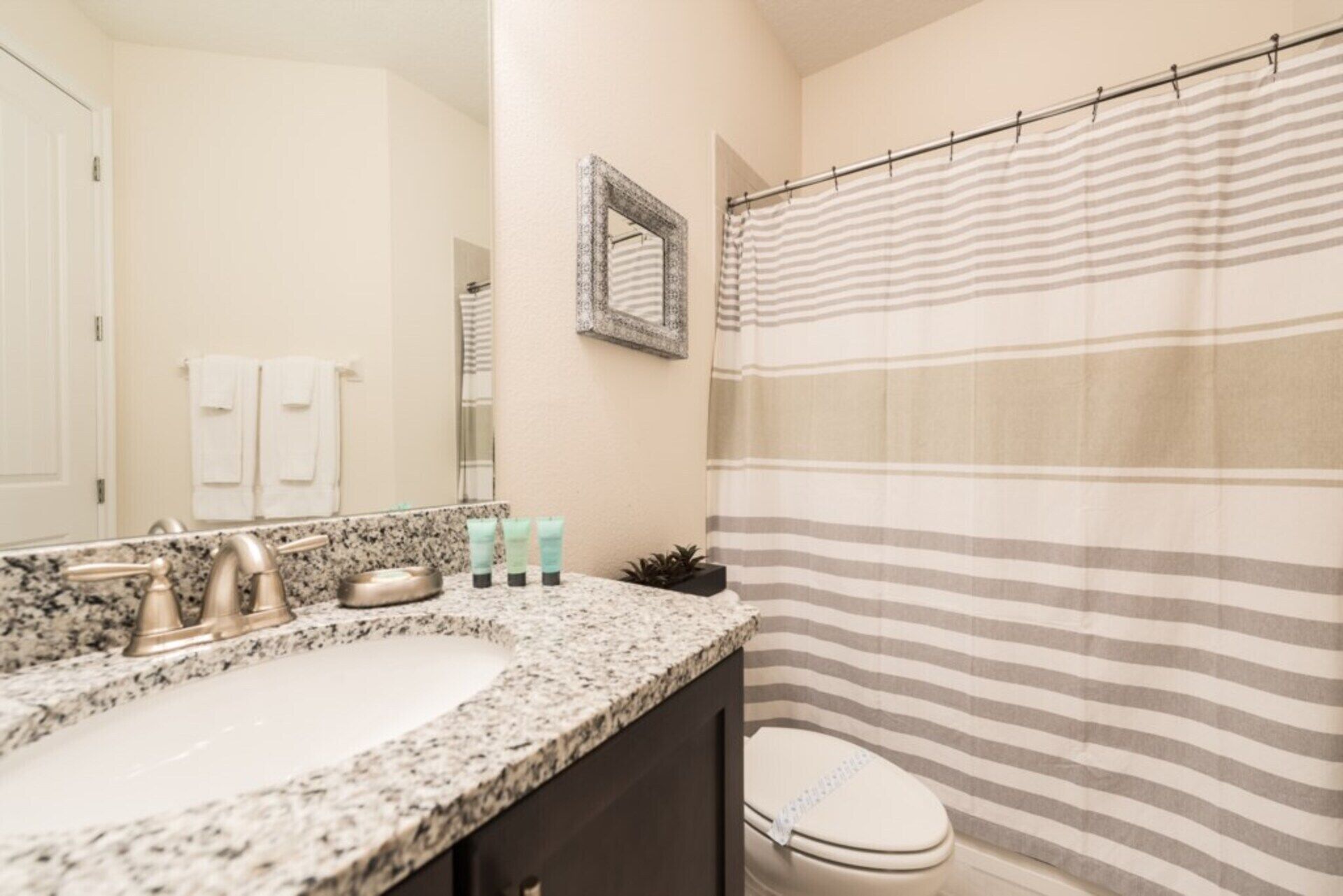 A bathroom with a granite countertop sink, a toilet, and a striped shower curtain.