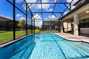 A swimming pool with a glass enclosure, surrounded by a patio area and a view of residential buildings. - Villa in Champions Gate 1128 (Davenport)