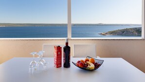 Ett bord med en fruktskål, vinglas och en vinflaska, med utsikt över kusten.