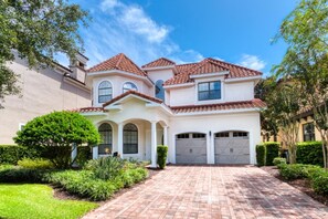 A two-story house with a red-tiled roof, a driveway, and a well-maintained garden.
