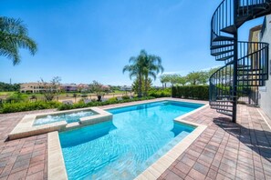 A swimming pool with a hot tub, surrounded by a brick patio, and a spiral staircase leading to an upper level.
