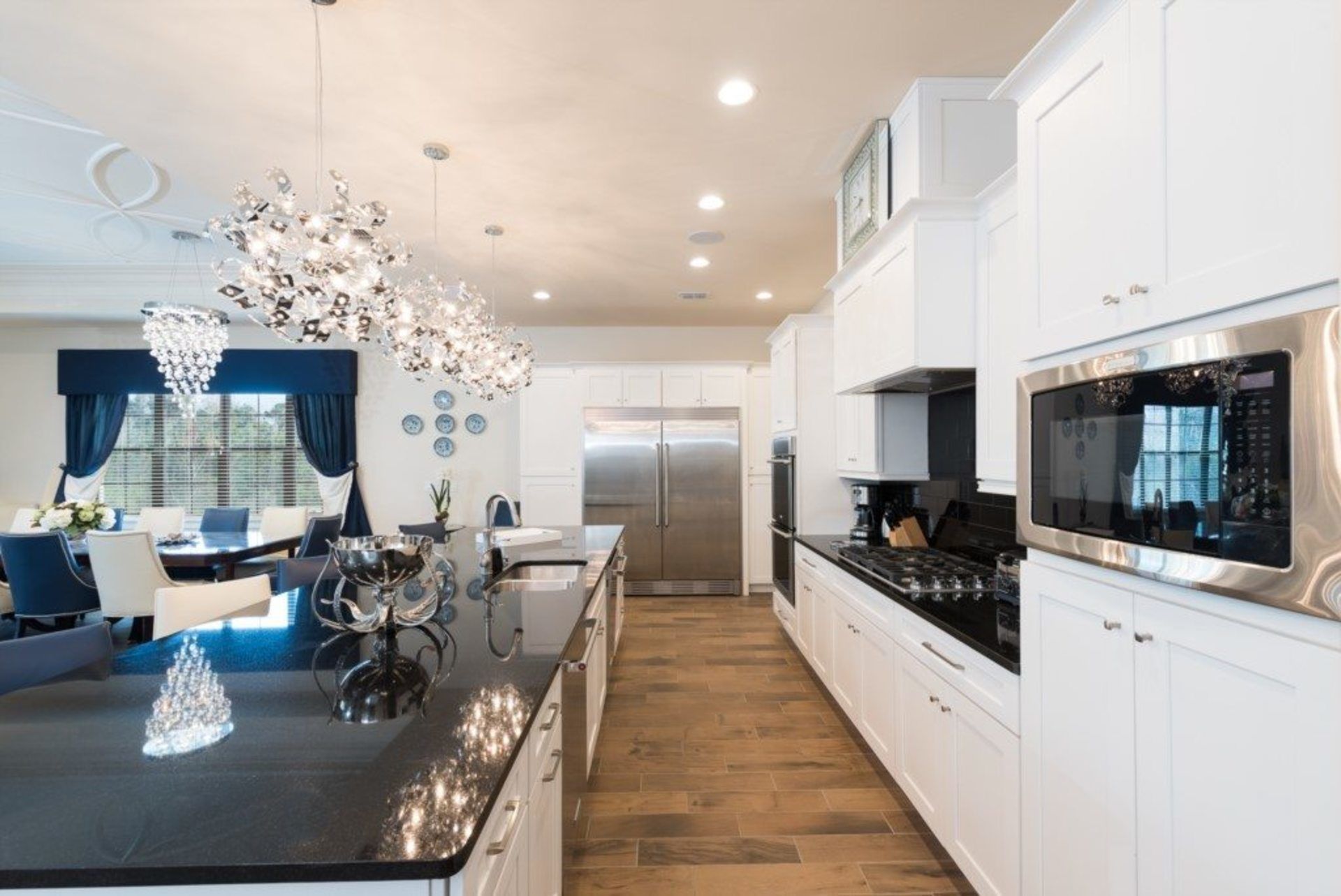 A modern kitchen with white cabinetry, stainless steel appliances, and a central island with a chandelier.